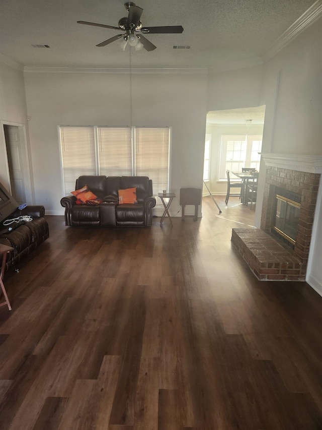 living room with visible vents, a brick fireplace, crown molding, wood finished floors, and a textured ceiling