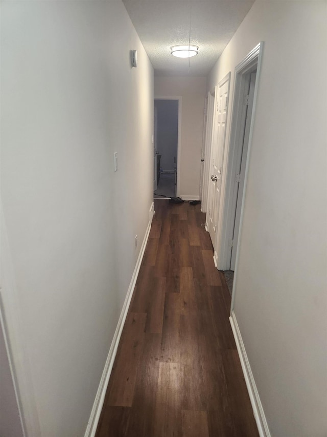 corridor with baseboards, dark wood-style flooring, and a textured ceiling