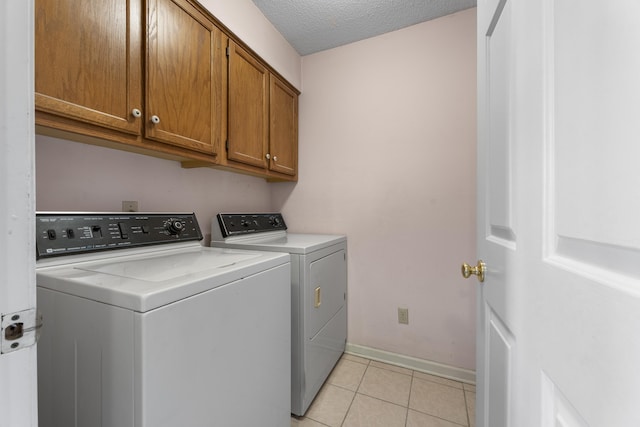 clothes washing area with light tile patterned floors, baseboards, cabinet space, a textured ceiling, and washer and clothes dryer