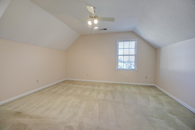 additional living space featuring visible vents, baseboards, light colored carpet, lofted ceiling, and a textured ceiling