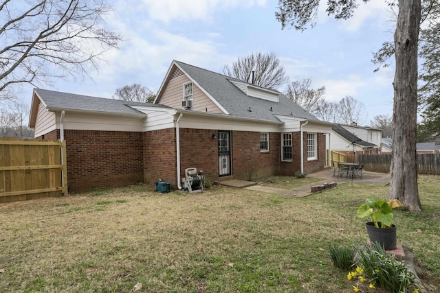 rear view of property with brick siding, a shingled roof, fence, a lawn, and a patio area