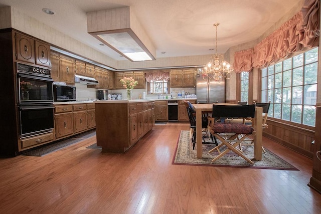 kitchen with under cabinet range hood, black appliances, light countertops, and hardwood / wood-style floors