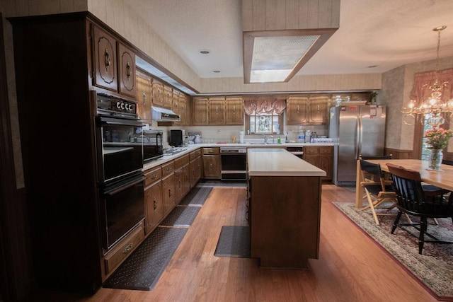 kitchen featuring wood finished floors, freestanding refrigerator, a sink, light countertops, and under cabinet range hood