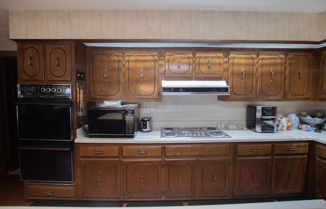 kitchen featuring backsplash, under cabinet range hood, light countertops, brown cabinetry, and black appliances