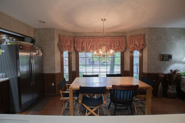 dining area featuring a chandelier, a wainscoted wall, wooden walls, and wood finished floors