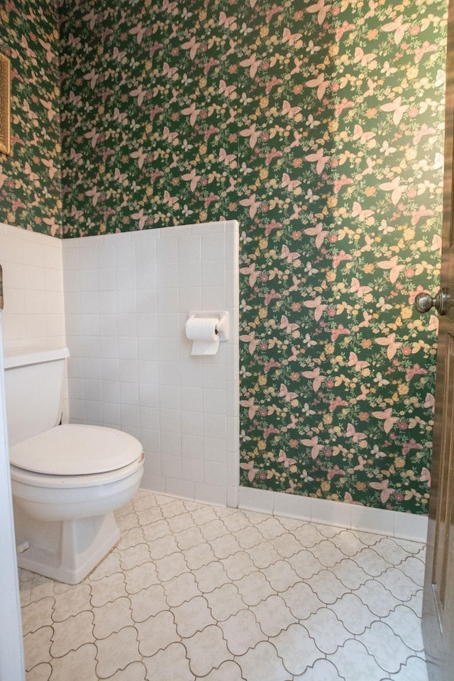 bathroom with wallpapered walls, toilet, and tile walls