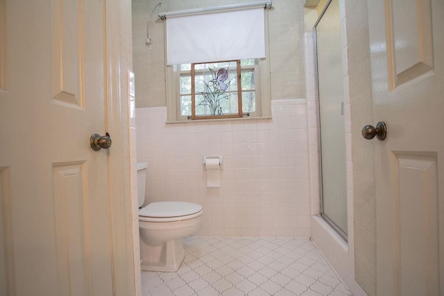 bathroom featuring a shower with shower door, toilet, and tile walls