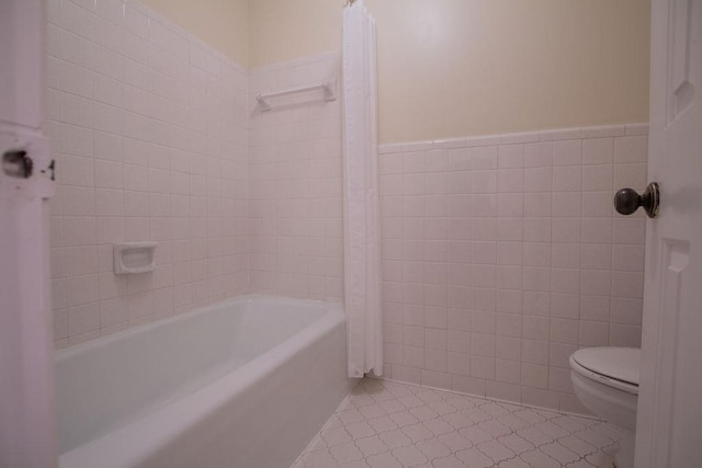 bathroom featuring tile walls, toilet, shower / tub combo with curtain, and wainscoting