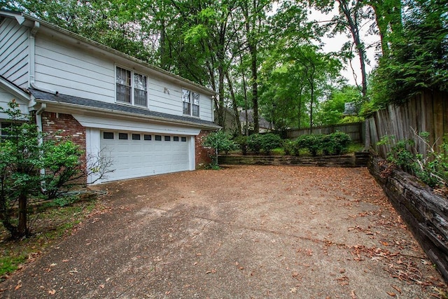 exterior space with a garage, brick siding, driveway, and fence