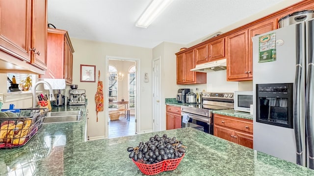 kitchen with a sink, dark stone countertops, under cabinet range hood, and stainless steel appliances