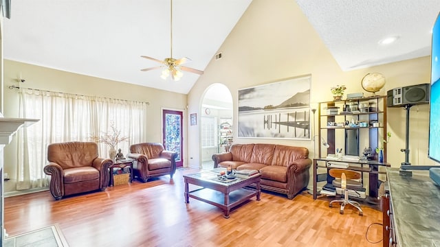 living room with ceiling fan, high vaulted ceiling, wood finished floors, arched walkways, and a textured ceiling