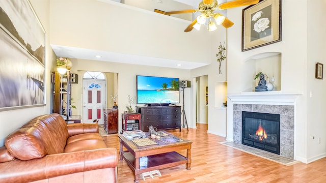 living room featuring ceiling fan, a high ceiling, wood finished floors, and a tile fireplace