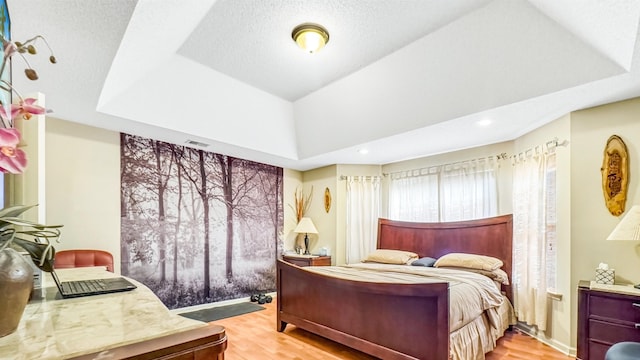 bedroom with recessed lighting, a raised ceiling, a textured ceiling, and light wood-style flooring