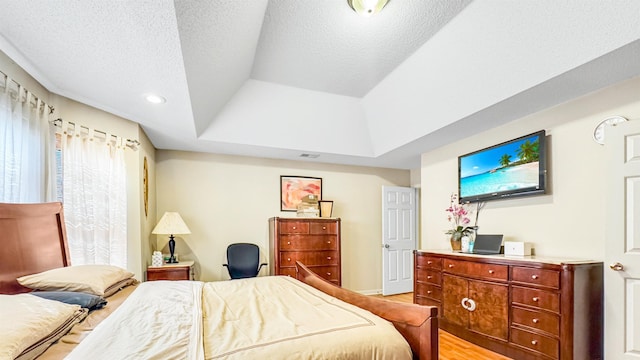 bedroom with visible vents, a tray ceiling, vaulted ceiling, light wood-style floors, and a textured ceiling