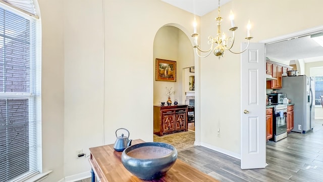 dining room featuring arched walkways, an inviting chandelier, baseboards, and wood finished floors