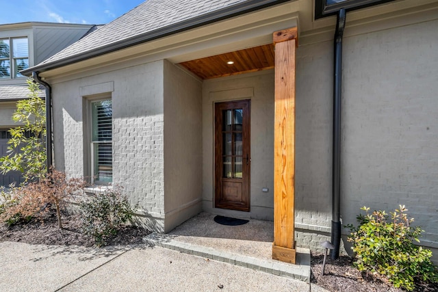 property entrance featuring brick siding and a shingled roof