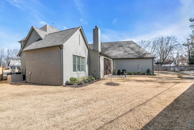 rear view of house with a shingled roof, stucco siding, a chimney, and fence