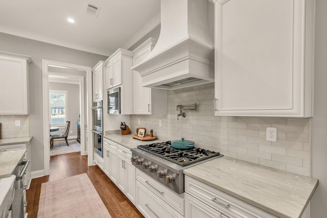 kitchen with dark wood-style floors, visible vents, custom exhaust hood, white cabinets, and appliances with stainless steel finishes