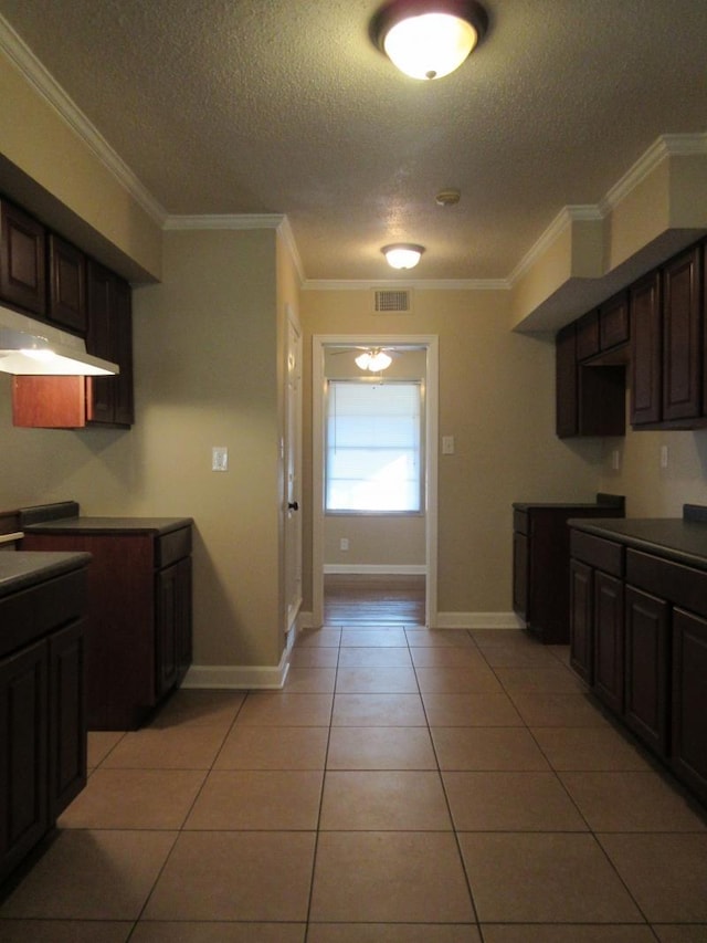 kitchen with visible vents, under cabinet range hood, a textured ceiling, crown molding, and light tile patterned floors