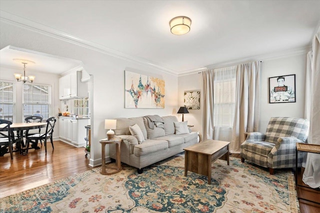 living room with light wood-type flooring, ornamental molding, arched walkways, baseboards, and a chandelier