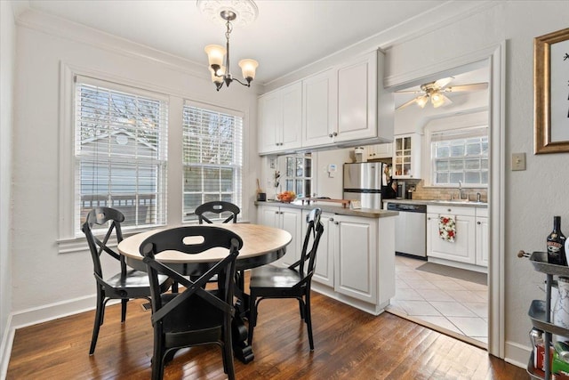 dining area featuring dark wood finished floors, crown molding, ceiling fan with notable chandelier, and baseboards