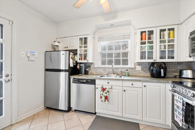 kitchen featuring light tile patterned floors, a sink, appliances with stainless steel finishes, white cabinetry, and tasteful backsplash