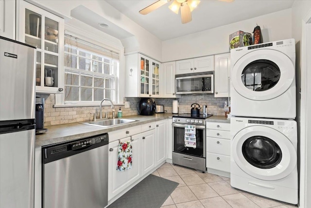 kitchen with tasteful backsplash, light tile patterned floors, stacked washer and clothes dryer, appliances with stainless steel finishes, and a sink