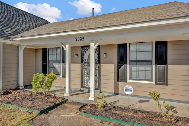 entrance to property with a porch and a shingled roof