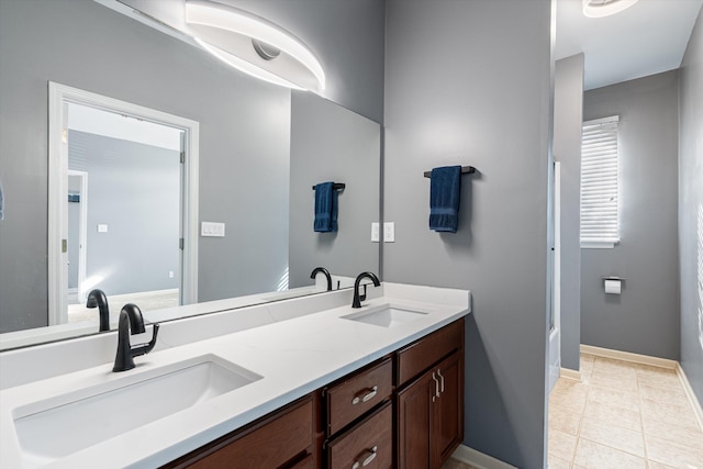 full bath with double vanity, baseboards, and a sink