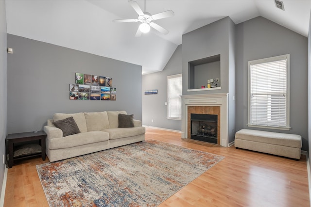 living area with a tiled fireplace, vaulted ceiling, visible vents, and wood finished floors