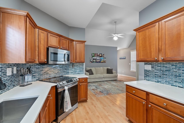 kitchen with open floor plan, brown cabinets, stainless steel appliances, a ceiling fan, and a sink