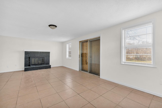 unfurnished living room with light tile patterned flooring, a brick fireplace, and baseboards