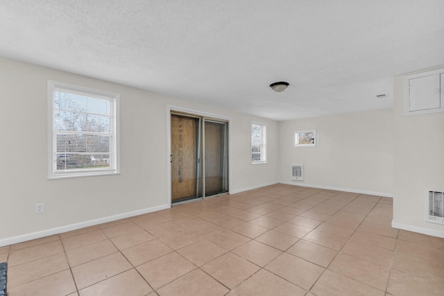 empty room featuring visible vents, baseboards, a textured ceiling, and light tile patterned flooring