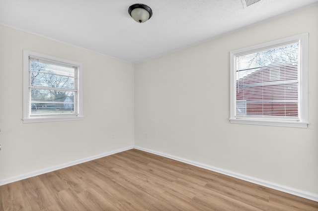 empty room featuring baseboards, a textured ceiling, a healthy amount of sunlight, and wood finished floors