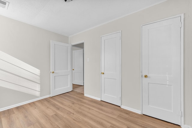 unfurnished bedroom with baseboards, visible vents, light wood finished floors, and a textured ceiling