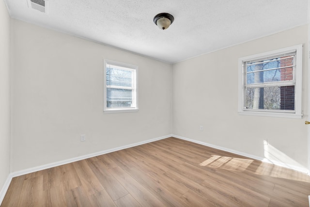 spare room with baseboards, wood finished floors, visible vents, and a textured ceiling