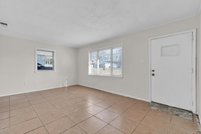 empty room featuring light tile patterned flooring, visible vents, a textured ceiling, and baseboards