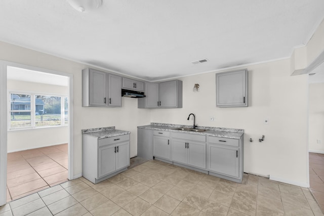 kitchen with visible vents, gray cabinets, a sink, under cabinet range hood, and light tile patterned floors