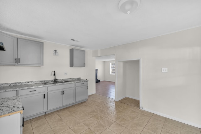 kitchen with visible vents, gray cabinets, a sink, light countertops, and baseboards