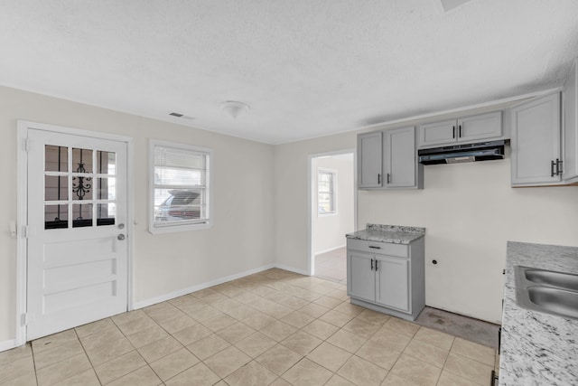 kitchen featuring under cabinet range hood, light tile patterned floors, gray cabinetry, and light countertops