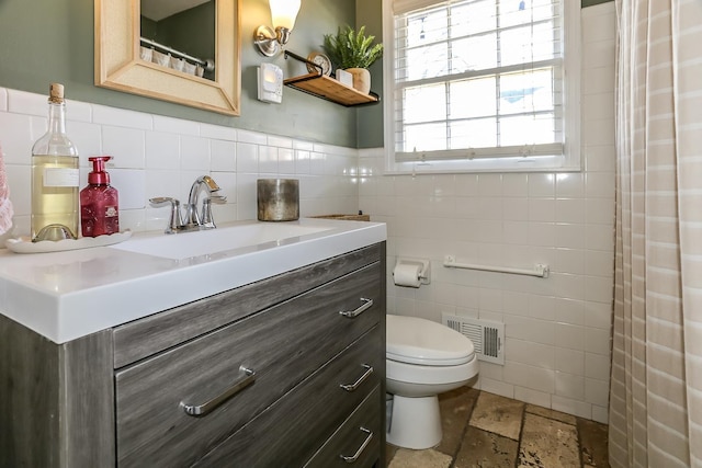 bathroom featuring visible vents, toilet, stone tile flooring, tile walls, and vanity