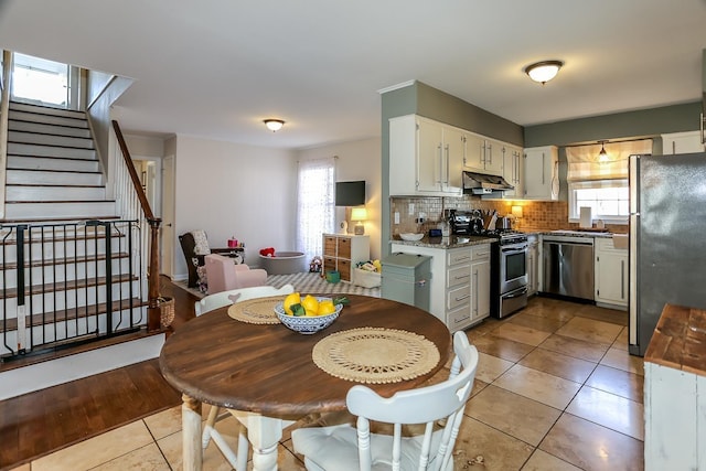 kitchen with light tile patterned flooring, stainless steel appliances, decorative backsplash, white cabinets, and under cabinet range hood