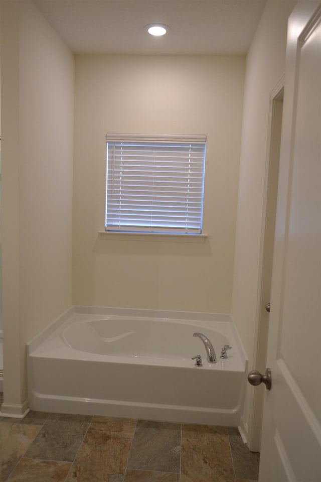 bathroom featuring a bath, recessed lighting, and stone finish floor