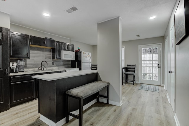 kitchen featuring a sink, freestanding refrigerator, light countertops, white microwave, and dark cabinets