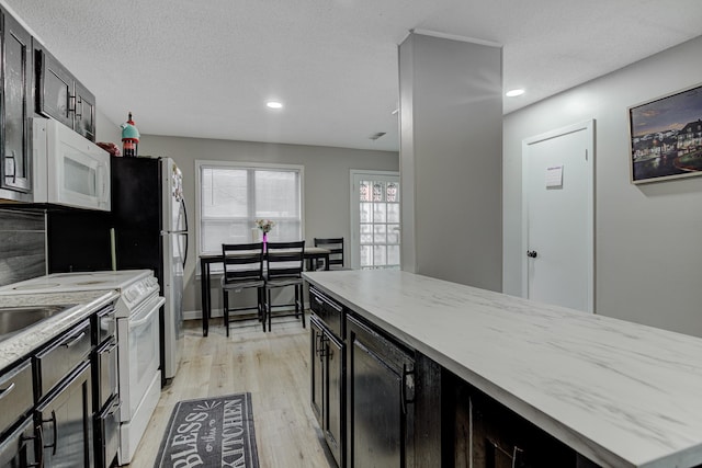 kitchen with dark cabinetry, white appliances, light stone counters, and light wood-type flooring