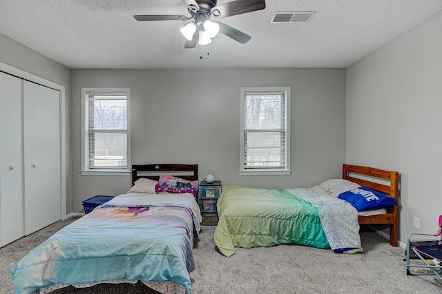 carpeted bedroom with visible vents, a textured ceiling, a closet, baseboards, and ceiling fan