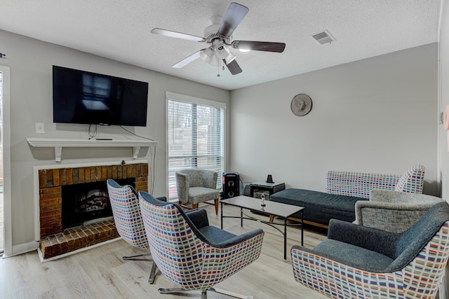 living area featuring visible vents, a textured ceiling, wood finished floors, a brick fireplace, and ceiling fan