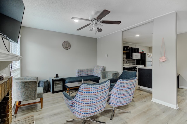 living room with light wood-style flooring, a ceiling fan, baseboards, and a textured ceiling