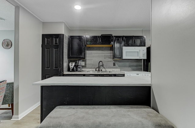 kitchen with white microwave, tasteful backsplash, light countertops, dark cabinetry, and a sink