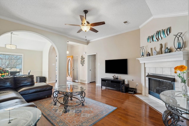 living room featuring visible vents, ornamental molding, a tiled fireplace, wood finished floors, and lofted ceiling